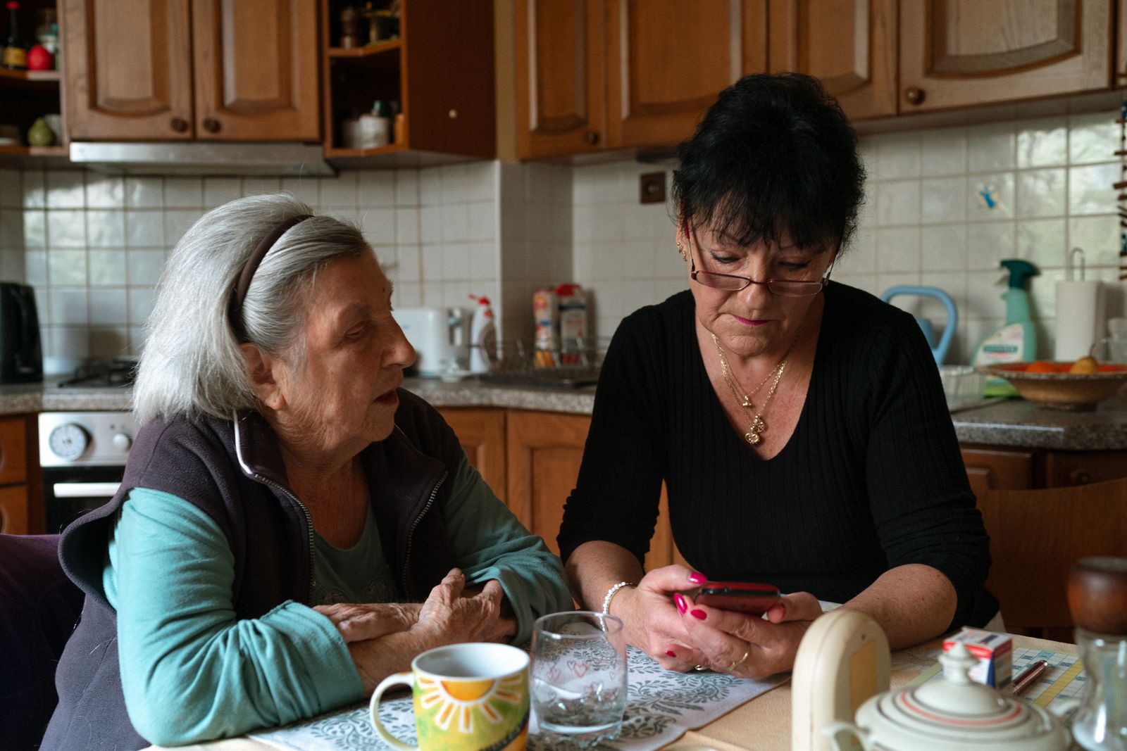 A woman caregiver helping an older woman use a phone at her kitchen table